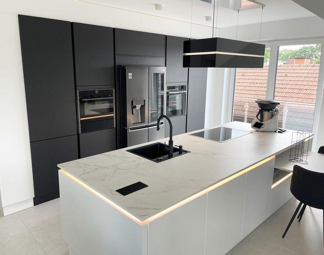 Moderne Küche mit Marmorinsel, Kochfeld, schwarzem Spülbecken und eleganter Beleuchtung.