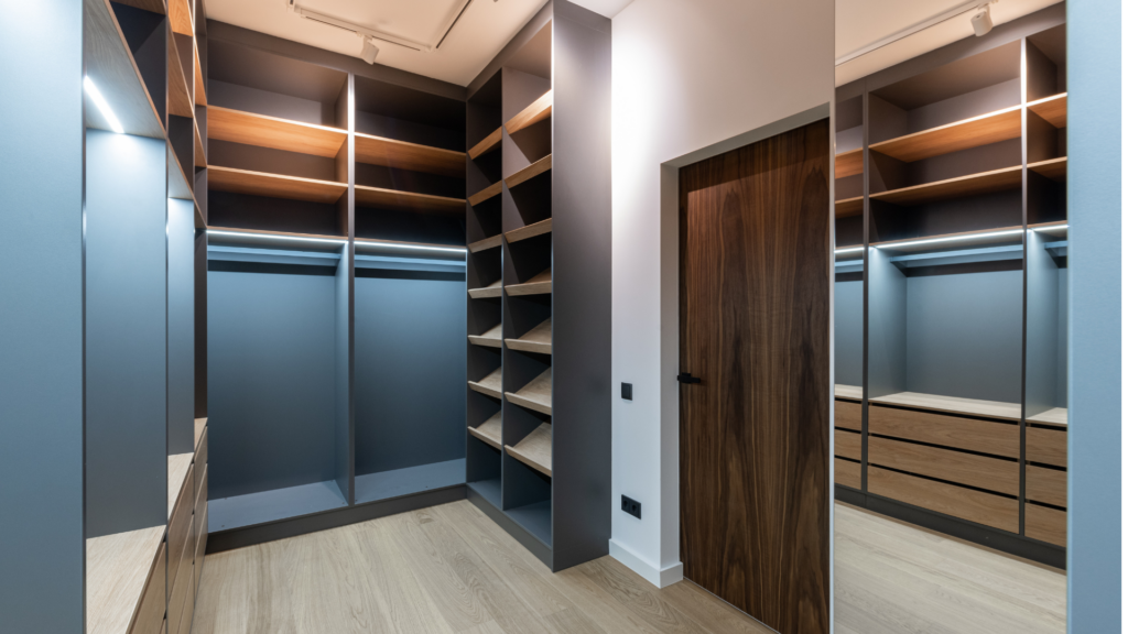 Moderner begehbarer Kleiderschrank mit grauen Regalen, Holzschubladen und heller Holzoptik am Boden.
