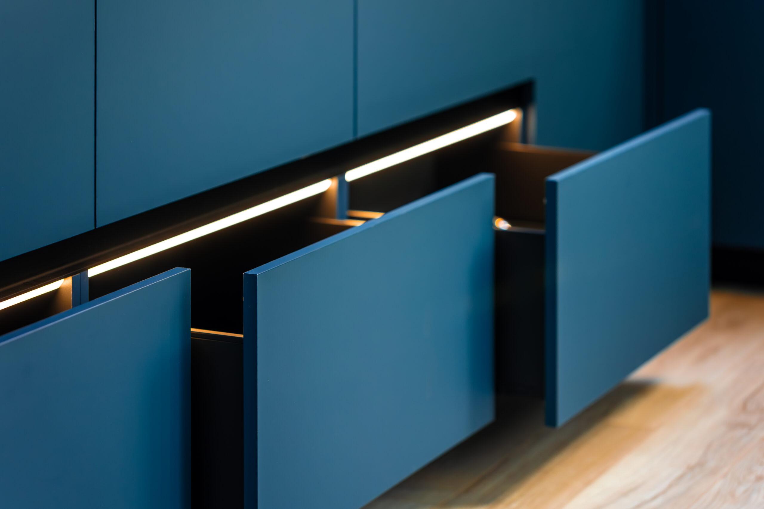 Moderne Küche mit drei geöffneten, blau beleuchteten Schubladen und warmem Holzboden.