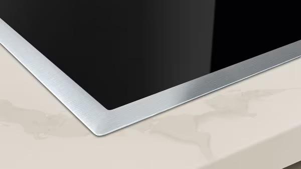 Ein modernes, schwarzes Kochfeld mit silbernem Rahmen auf einer beigen, matten Arbeitsplatte.