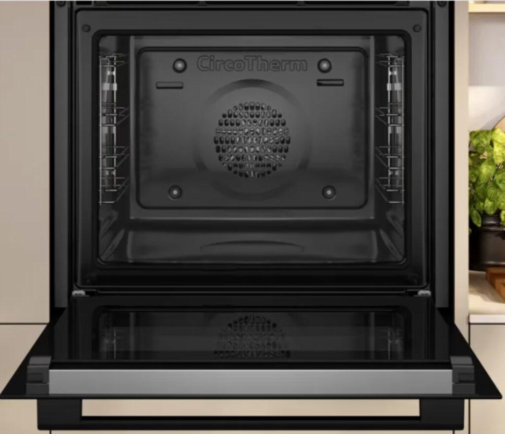 Moderner, offener Backofen in einer eleganten Küche mit grünen Pflanzen im Hintergrund.