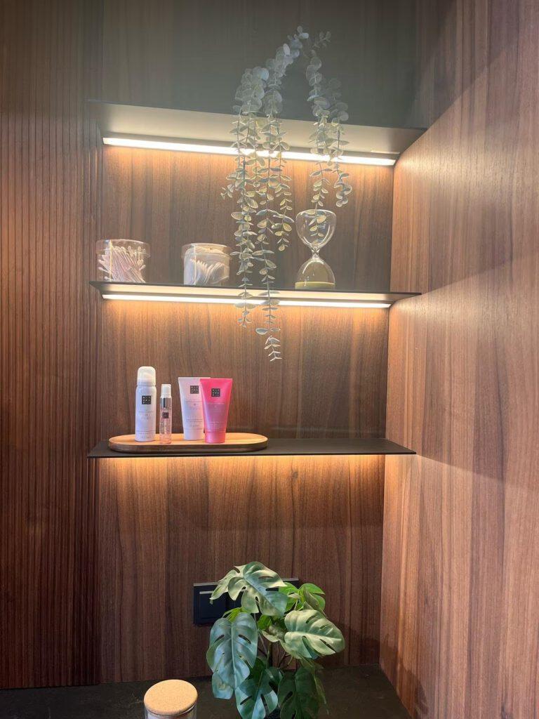 Ein stilvolles Regal mit Pflanzen, Kosmetikprodukten und warmem Licht in einem modernen Raum.