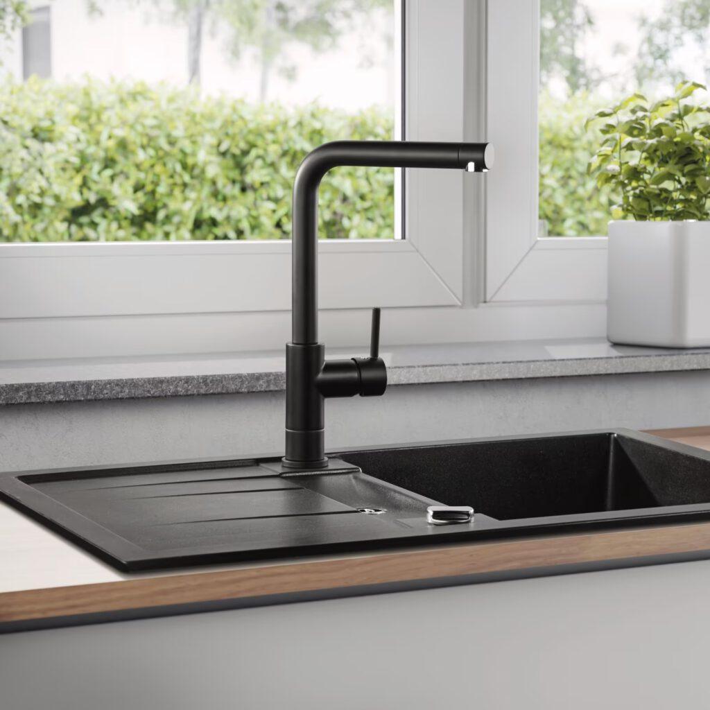 Moderne Küche mit schwarzem Wasserhahn und Spüle, viel Licht und einer Pflanze auf der Fensterbank.