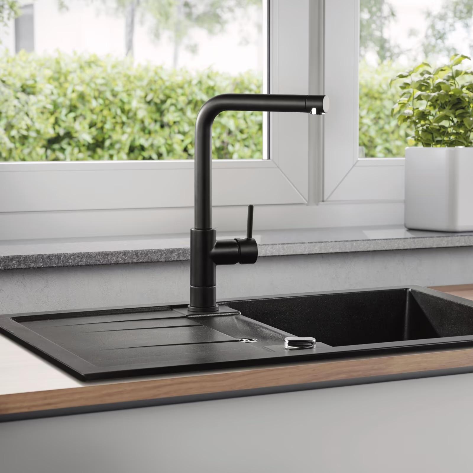 Moderne Küche mit schwarzem Wasserhahn und Spüle, viel Licht und einer Pflanze auf der Fensterbank.