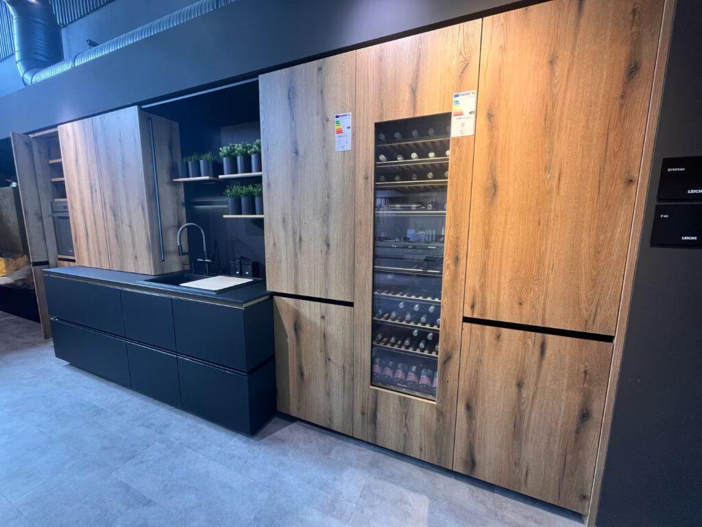 Moderne Küche mit Holzschränken, schwarzer Arbeitsplatte, Weinkühler und Pflanzen als Dekoration.