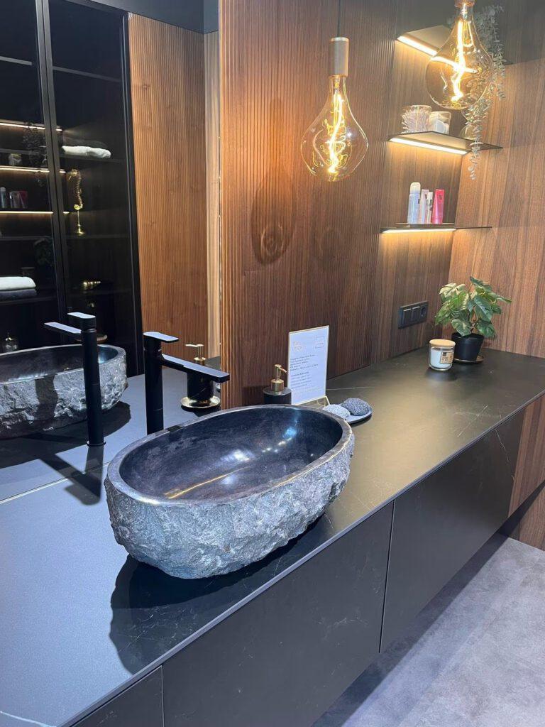 Modernes Badezimmer mit ovalem Steinwaschbecken, schwarzem Wasserhahn und hängenden Glühbirnen.