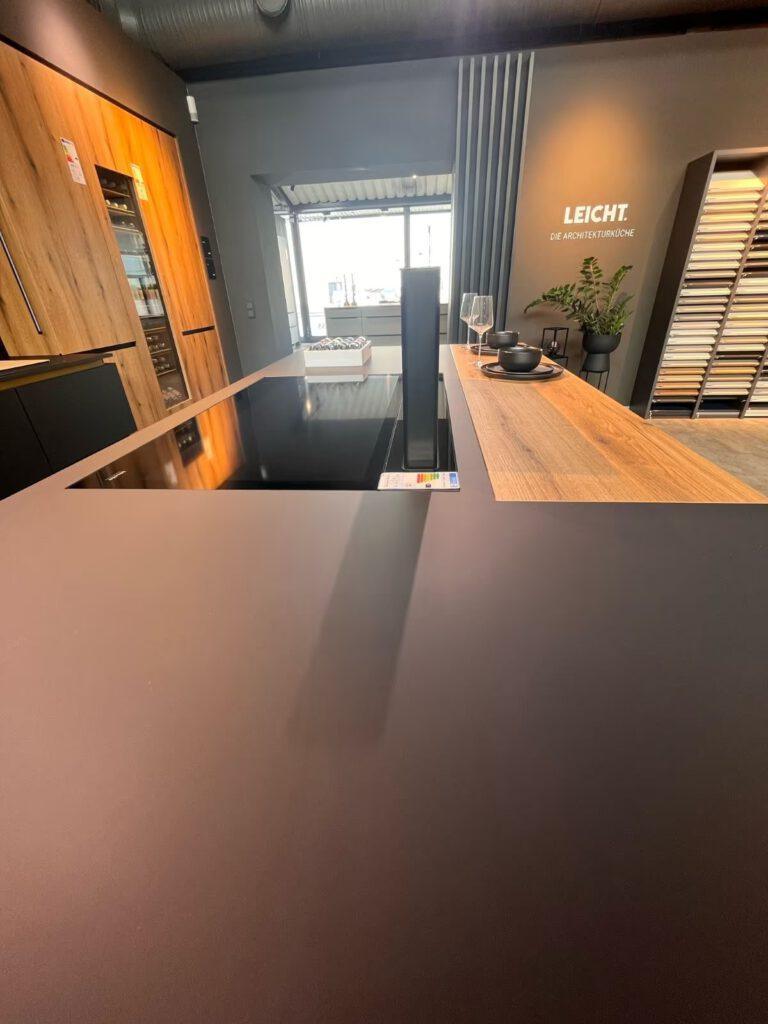 Moderne Küche mit dunkler Arbeitsfläche, Holzschränken, Weinkühlschrank und großem Fenster.