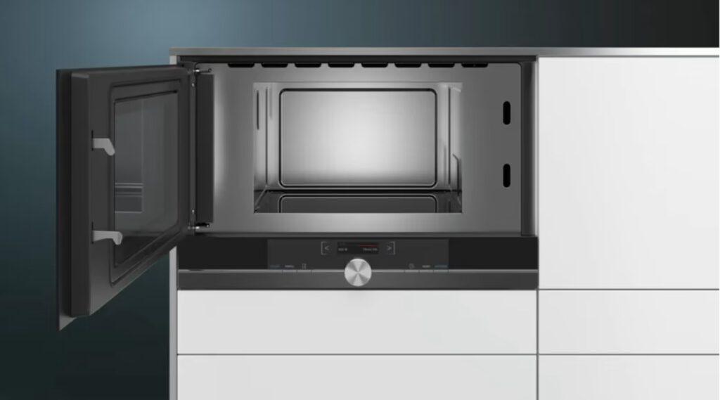 Moderne Einbau-Mikrowelle mit geöffneter Tür in weißem Küchenschrank, silberne und schwarze Akzente.