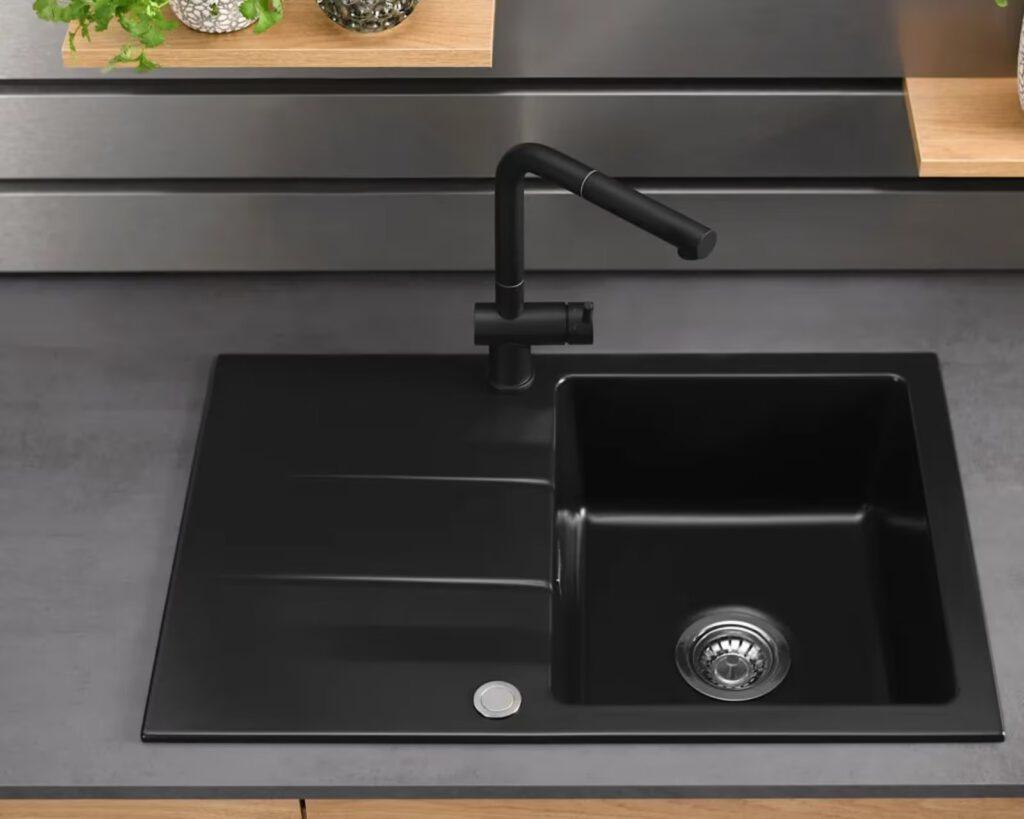 Moderne schwarze Küchenspüle mit schlichtem Wasserhahn, umgeben von Pflanzen in dekorativen Töpfen.
