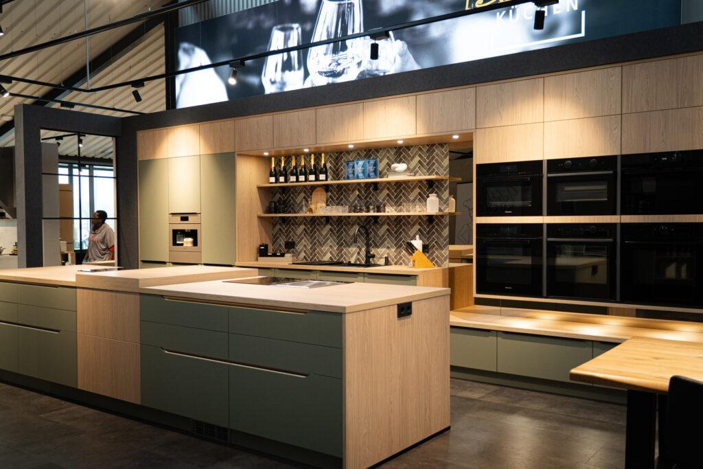 Moderne Küche mit Holzinsel, grünen Schränken, schwarzen Geräten und Fischgrätenfliesen.