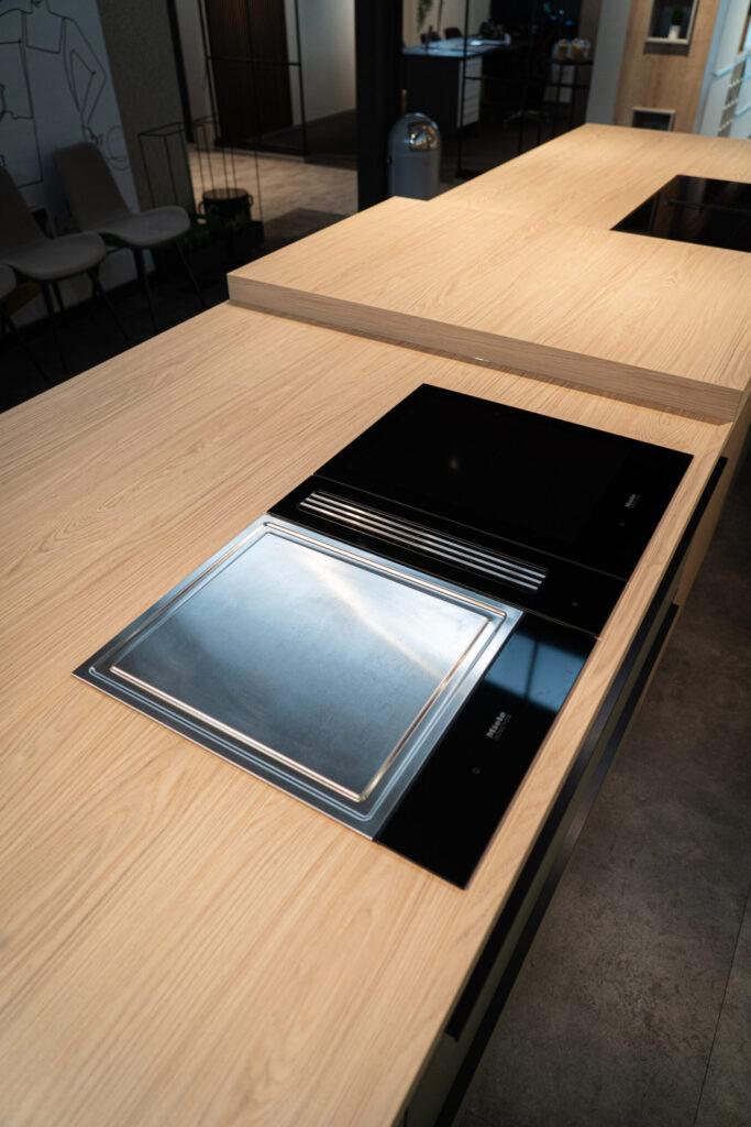 Moderne Küche mit heller Holzarbeitsplatte, schwarzen Kochfeldern und einer Edelstahlplatte.