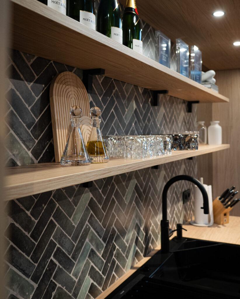 Moderne Küchenecke mit Holzregalen, Champagnerflaschen, Gläsern und einer schwarzen Spüle.