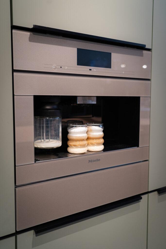 Eingebaute Miele-Kaffeemaschine mit zwei Gläsern Kaffee und Milchschaum in moderner Küche.