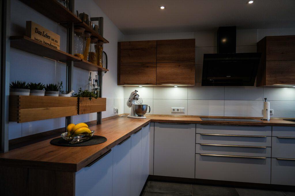 Moderne, aufgeräumte Küche mit weißen Schränken, Holzarbeitsplatten, Mixer und Teller mit Bananen.