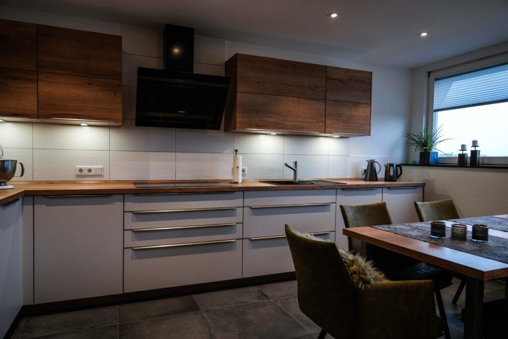 Moderne Küche mit Holz- und Weißtönen, Essbereich mit Holztisch und samtbezogenen Stühlen.