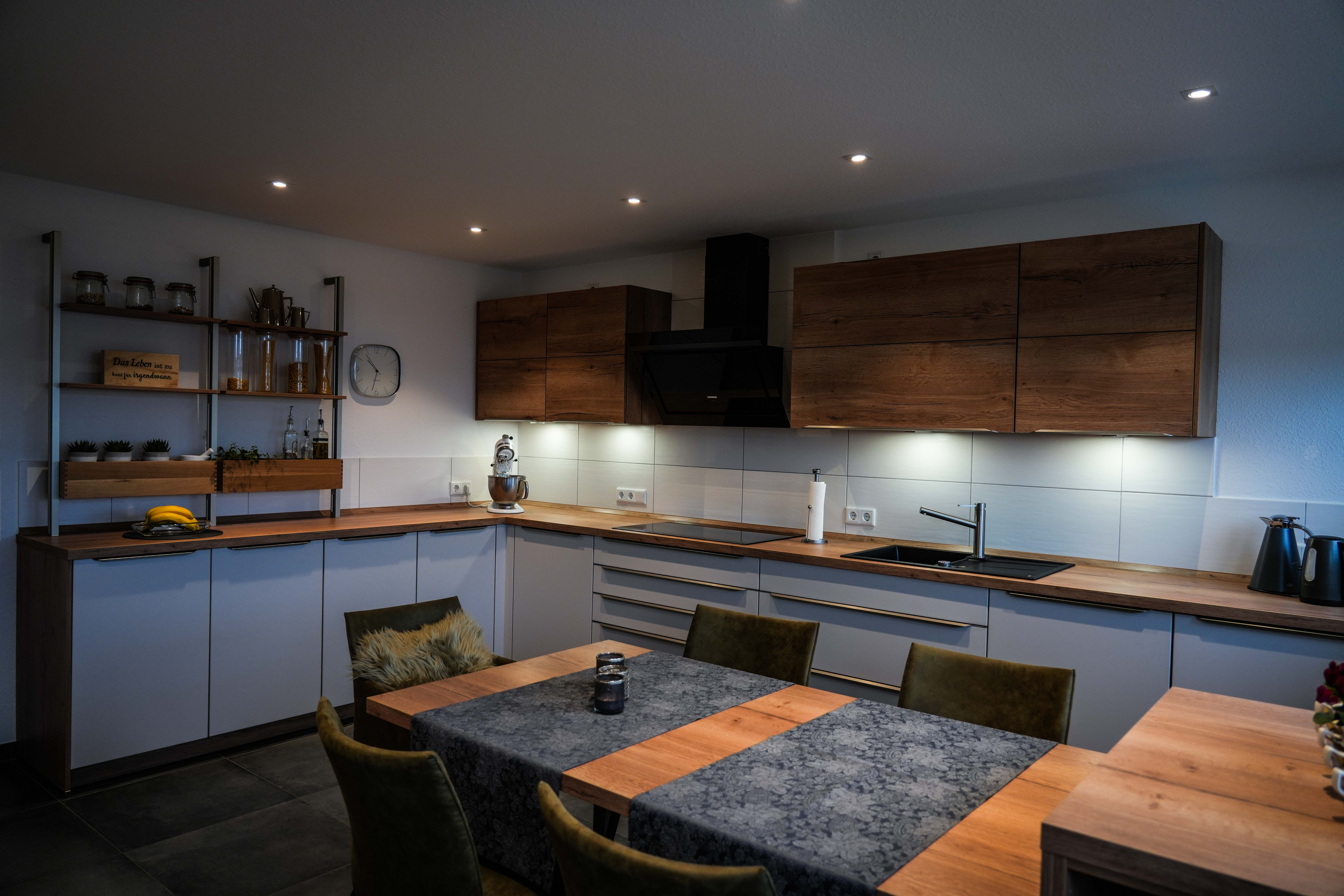 Moderne, einladende Küche mit Esstisch, Holzarbeitsplatten, weißen Schränken und warmem Licht.