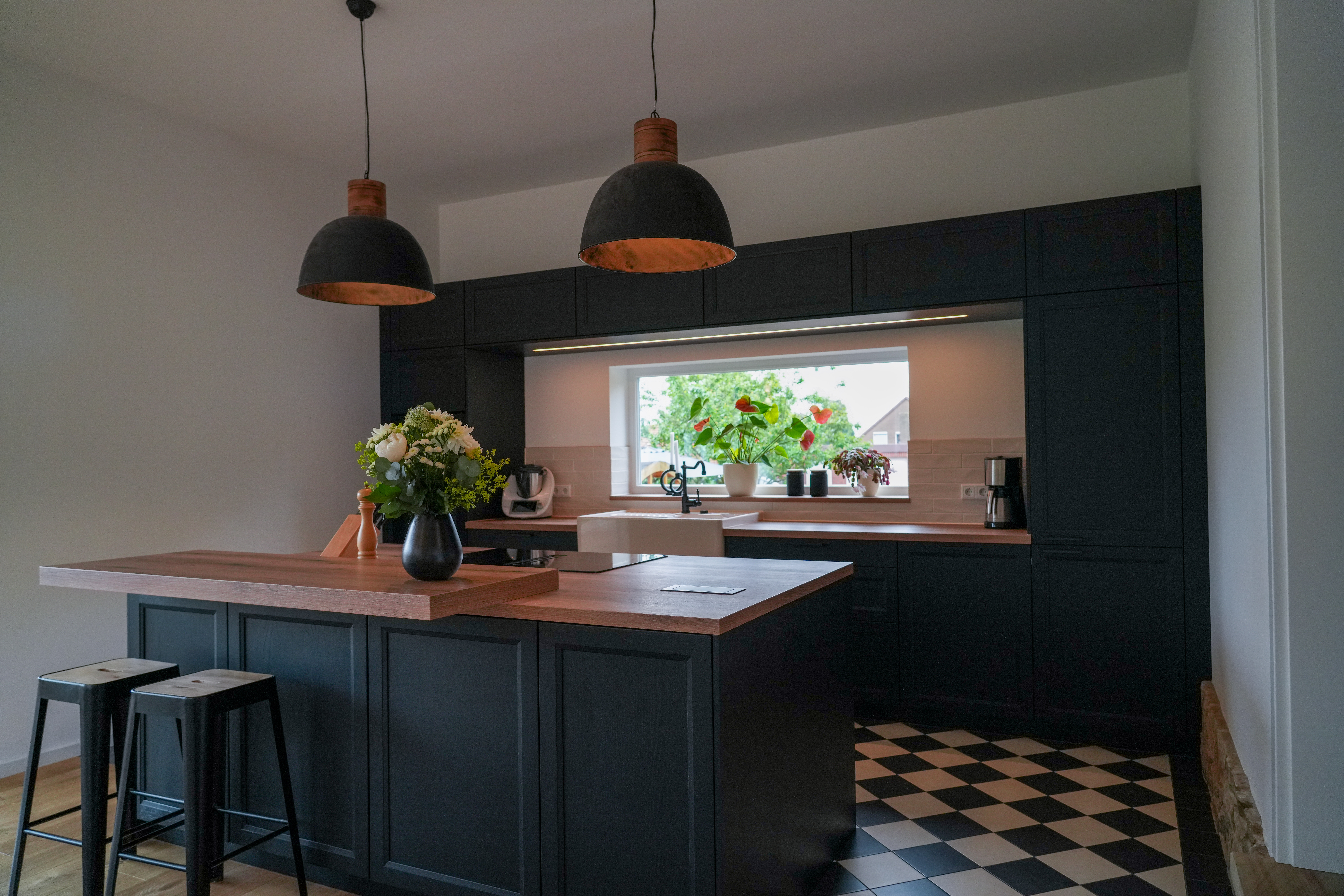 Moderne Küche mit schwarzer Einrichtung, Holzdetails und Pflanzen, die eine einladende Atmosphäre schafft.