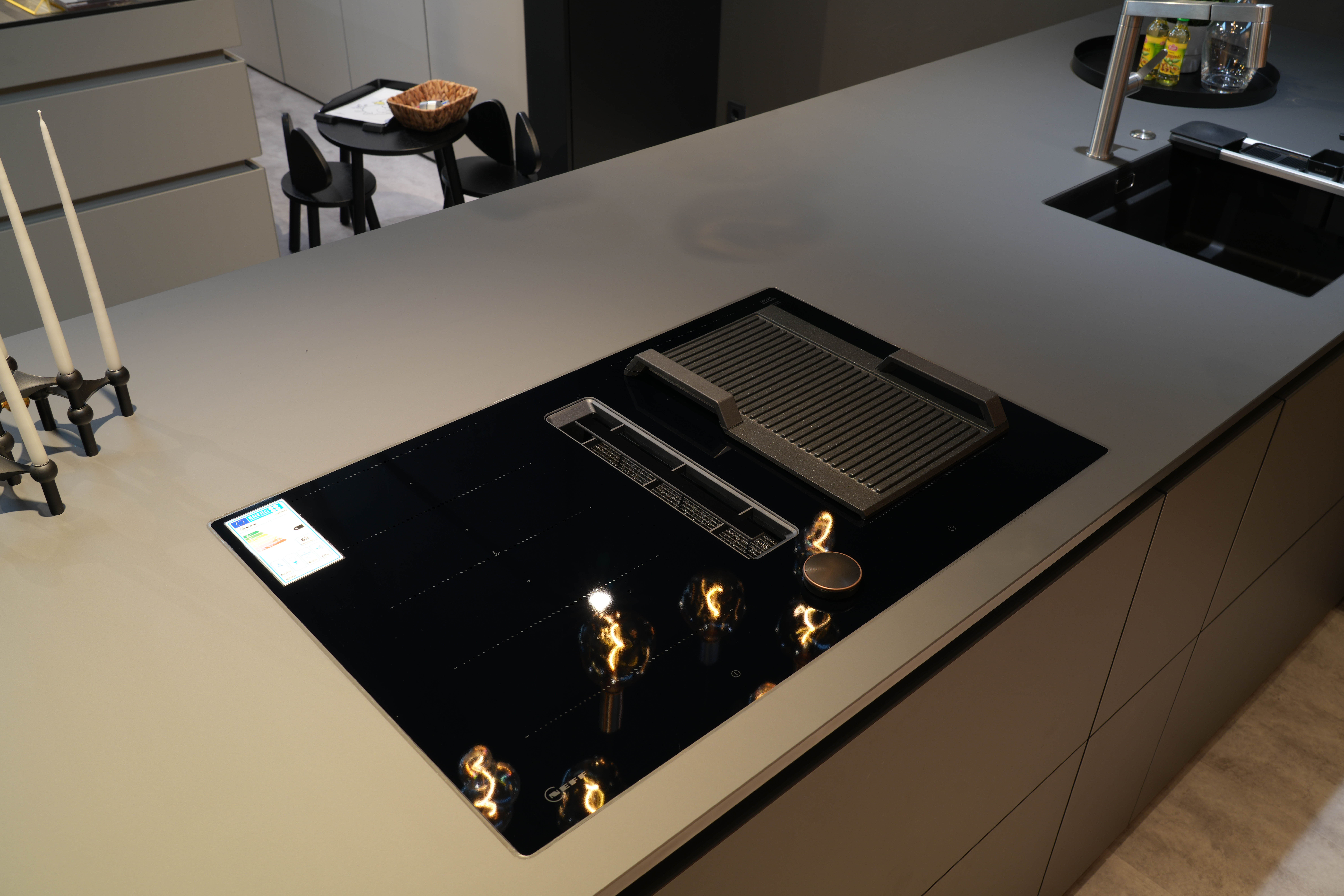 Moderne Küche mit grauer Arbeitsplatte, Induktionskochfeld, schwarzen Akzenten und warmem Licht.