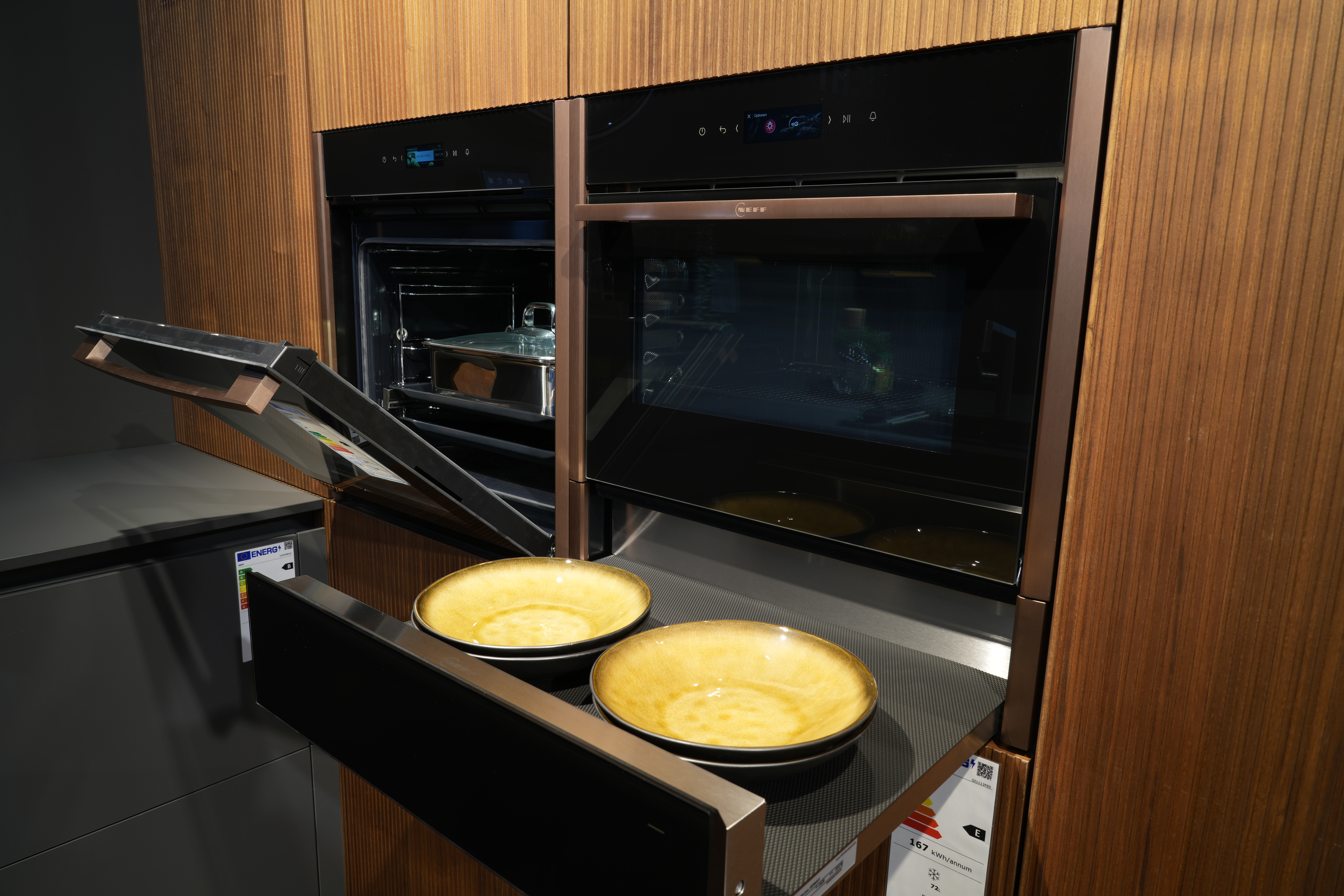 Moderne Küche mit zwei Einbauöfen, einer offen mit Bräter. Darunter gelbe Schalen auf Ablage.
