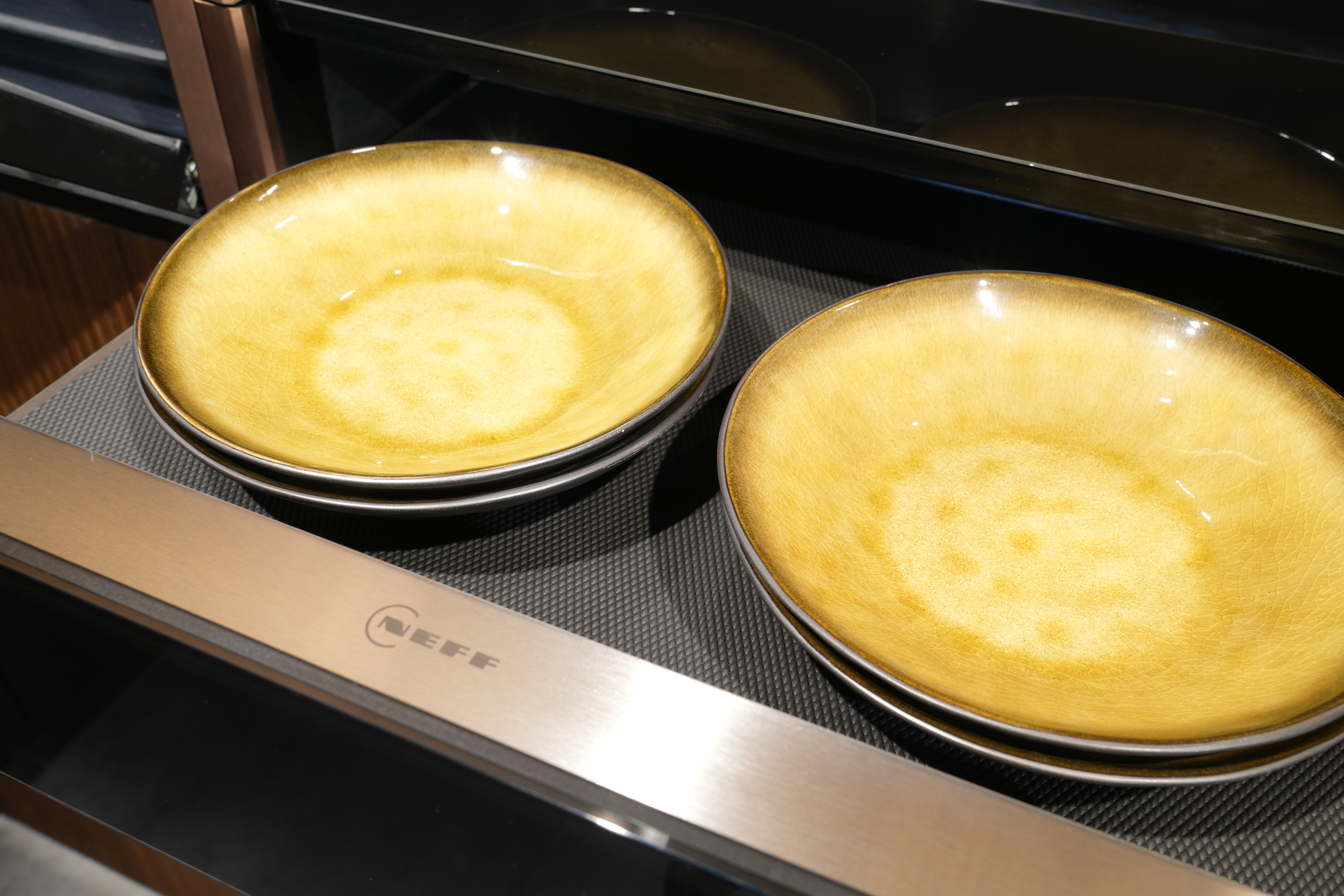 Zwei gelbe Teller auf dunkler Oberfläche, mit "NEFF"-Logo im Vordergrund, in moderner Küche.