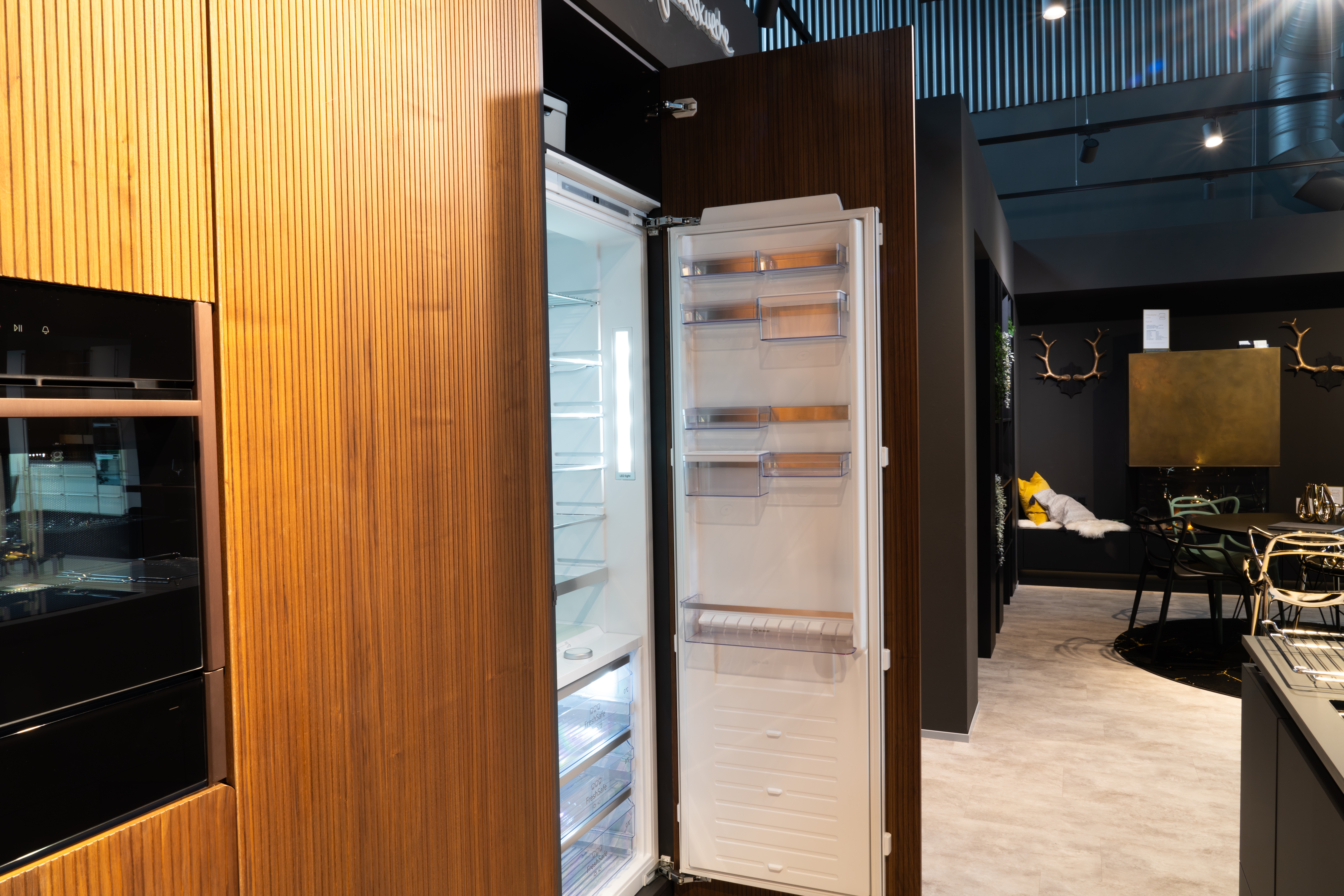 Moderne Küche mit offenem Kühlschrank, Einbaubackofen und stilvollem Essbereich im Hintergrund.