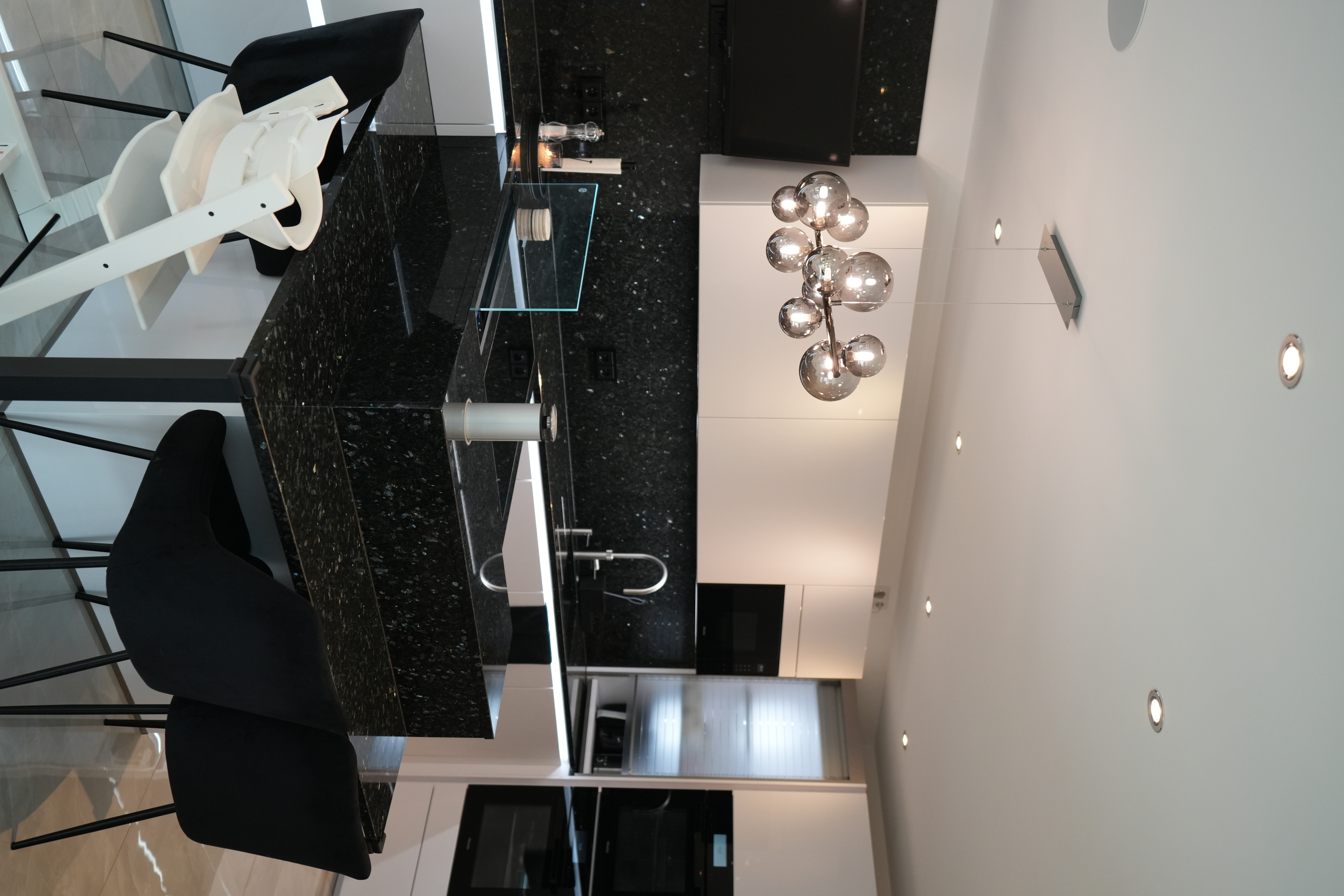 Moderne, aufgeräumte Küche in Schwarz-Weiß mit glänzender Arbeitsplatte und stilvollem Kronleuchter.