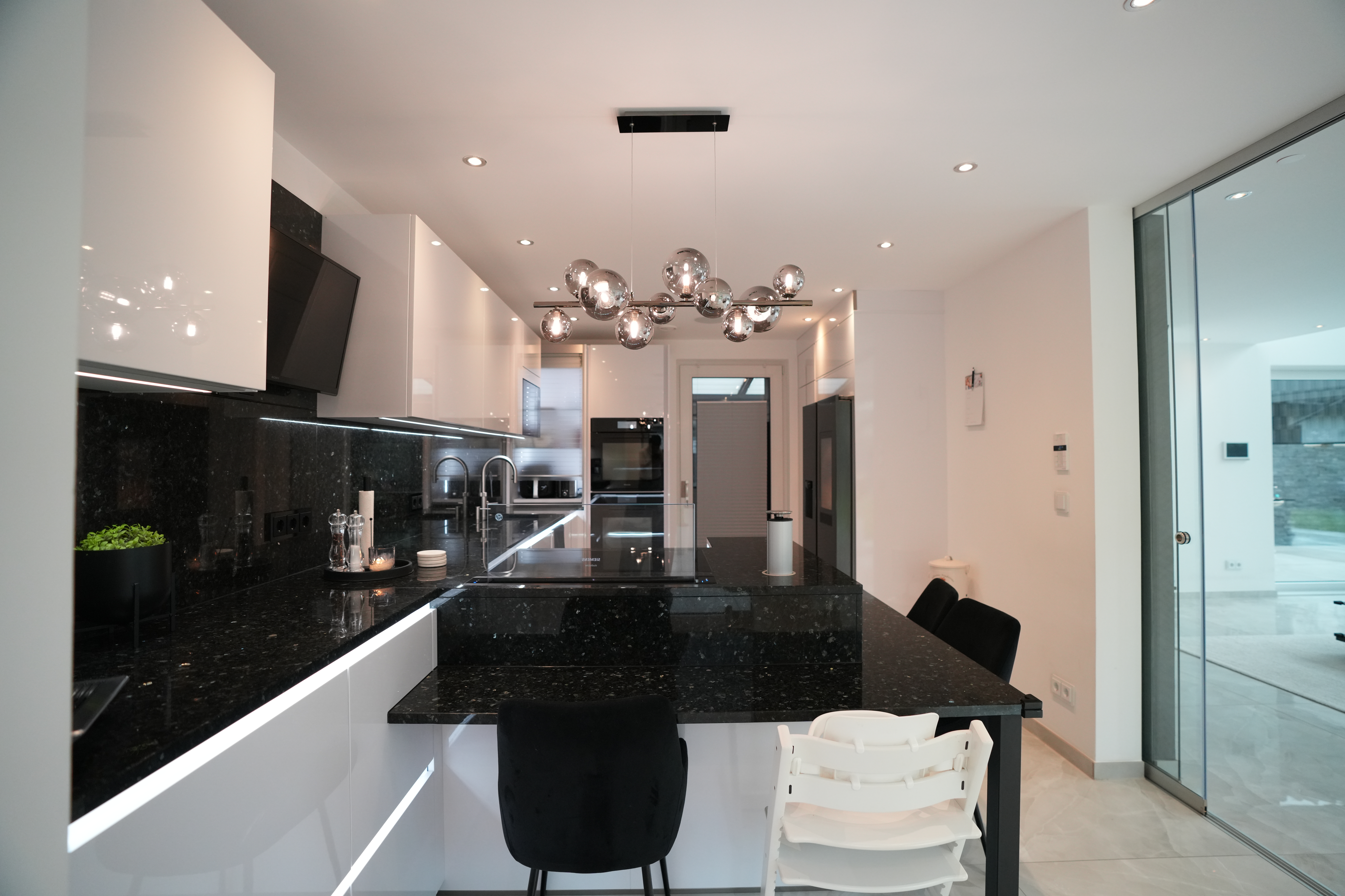 Moderne Küche mit schwarzer Insel, weißen Schränken, Hochstühlen und kugelförmigen Deckenleuchten.