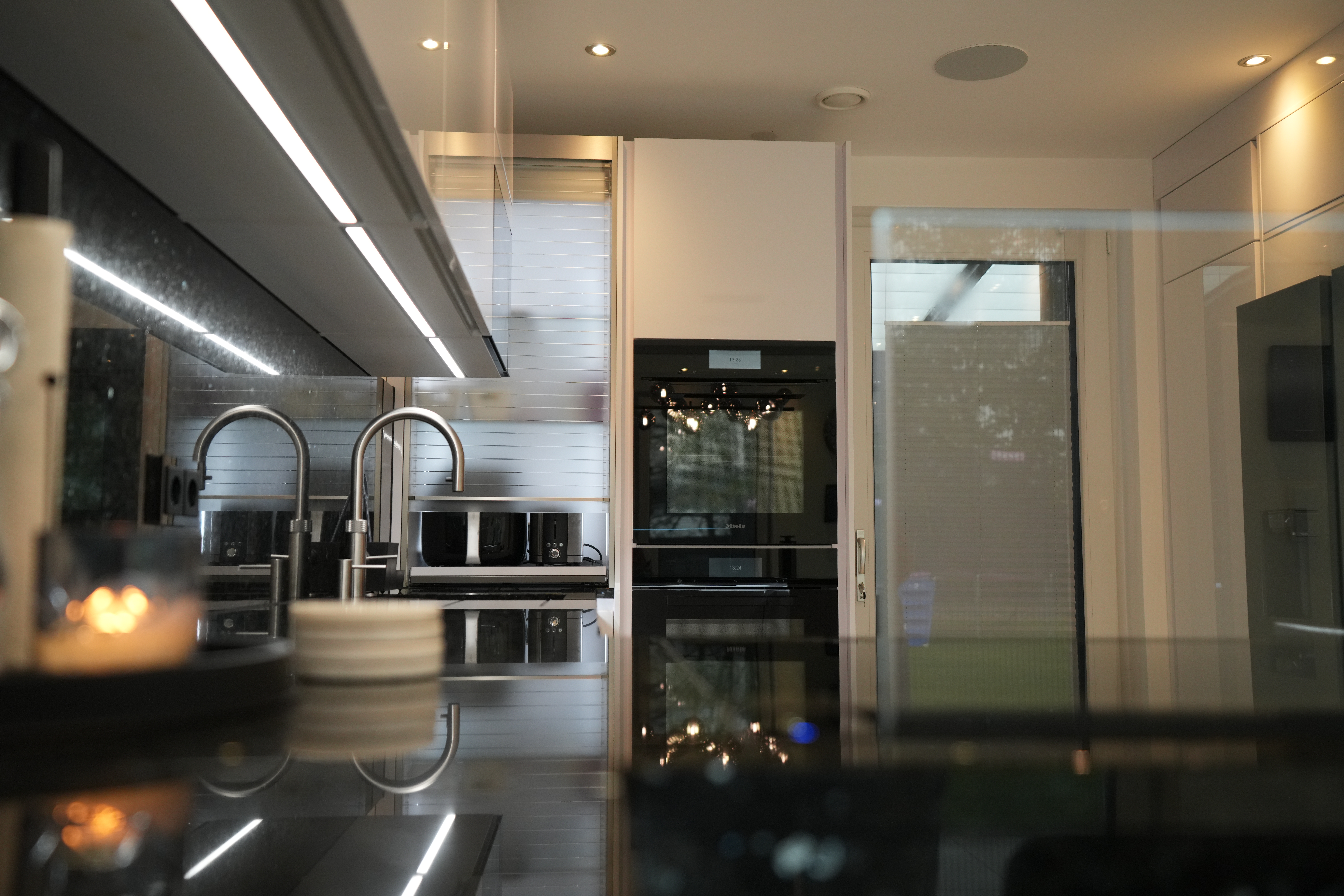 Moderne Küche mit Edelstahl-Wasserhähnen, integrierten Geräten und Kerzenlicht auf glänzender Arbeitsplatte.