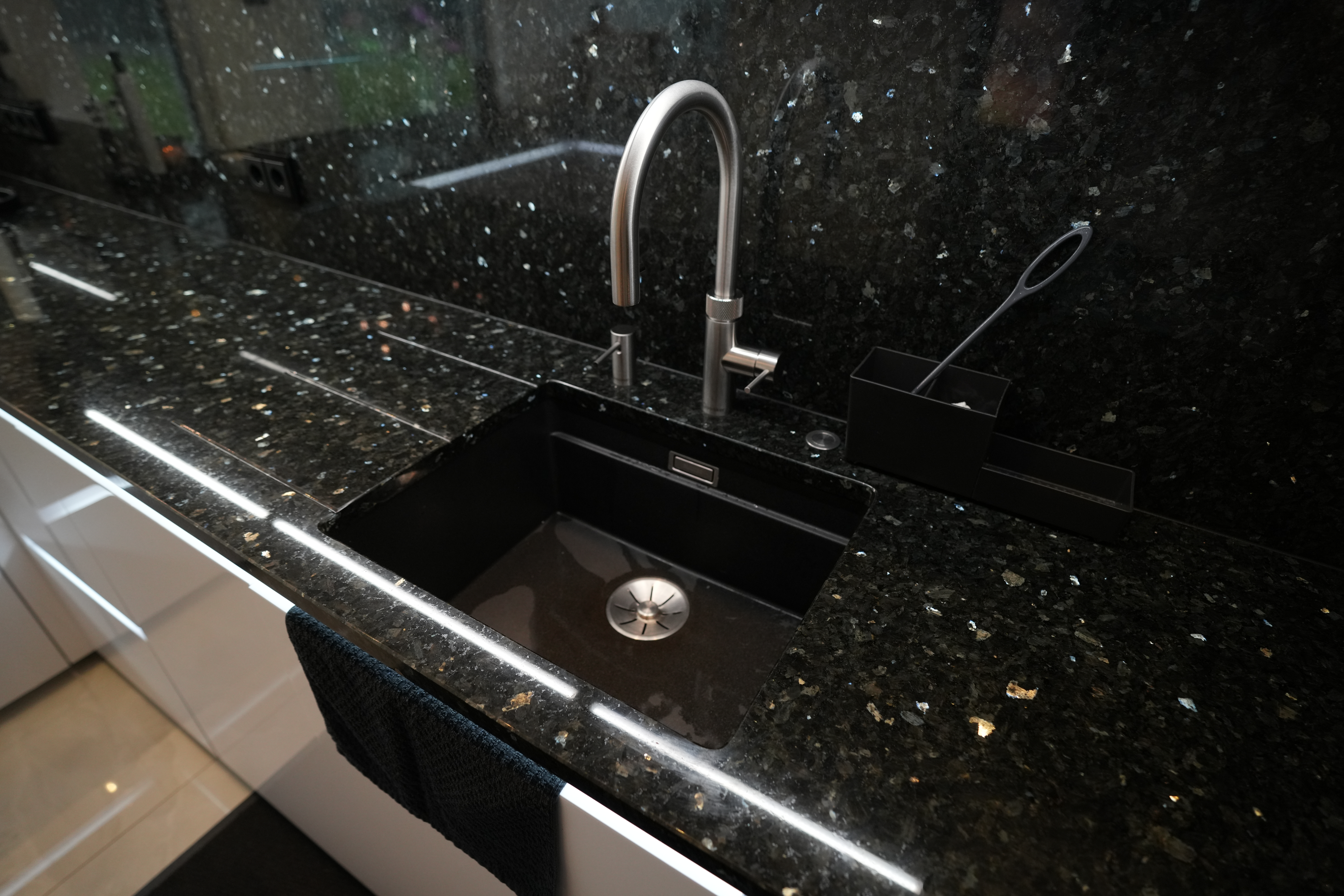 Moderne Küche mit schwarzer Spüle, Edelstahl-Wasserhahn und glänzender Arbeitsplatte.