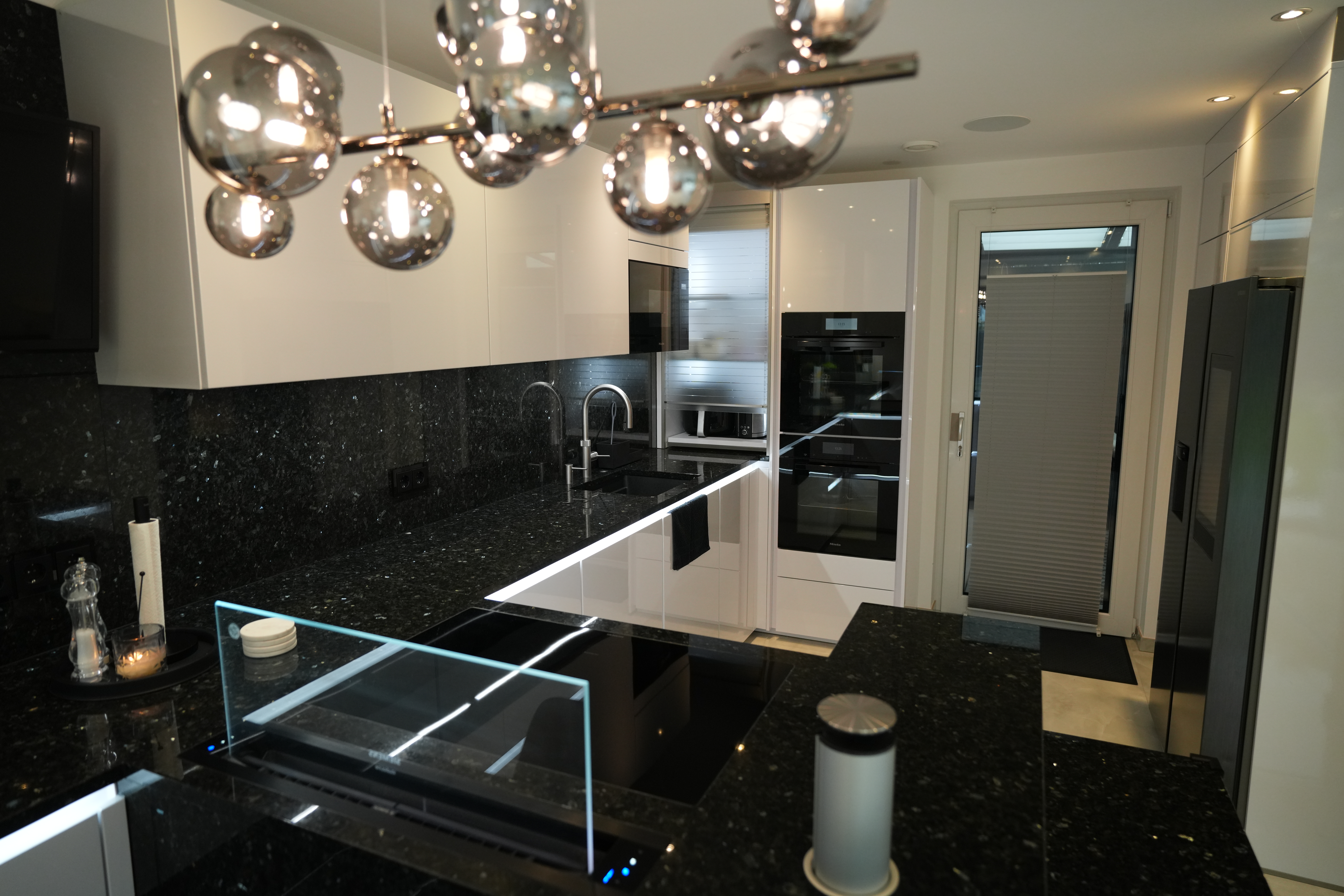 Moderne, unbenutzte Küche mit schwarzen Arbeitsplatten, weißen Schränken und glänzenden Oberflächen.