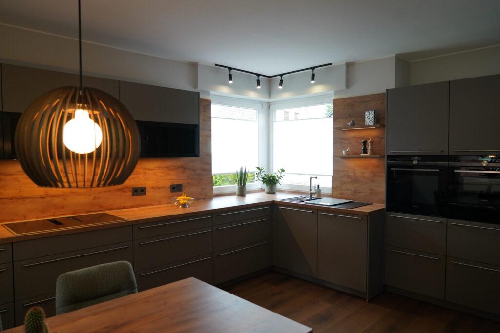 Moderne, aufgeräumte Küche mit grauen Schränken, Holzarbeitsplatte und dekorativen Pflanzen.