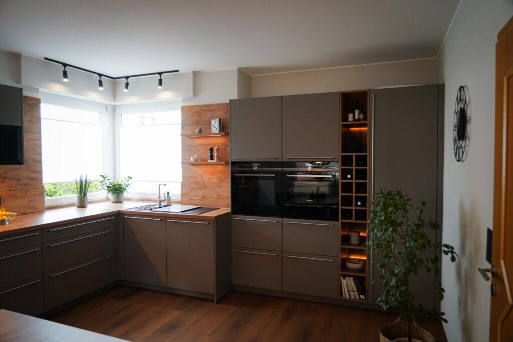 Moderne, aufgeräumte Küche mit grauen Schränken, Holzakzenten, Pflanzen und Einbaugeräten.