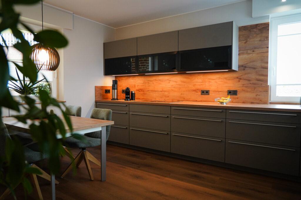 Moderne Küche mit grauen Schränken, Holzdetails, Esstisch und grünen Stühlen in gemütlicher Atmosphäre.