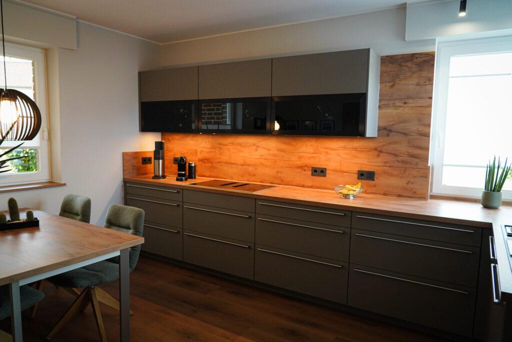 Moderne Küche in Grau und Holzoptik, mit Tisch, Kaffeemaschine und Pflanze, wirkt einladend.