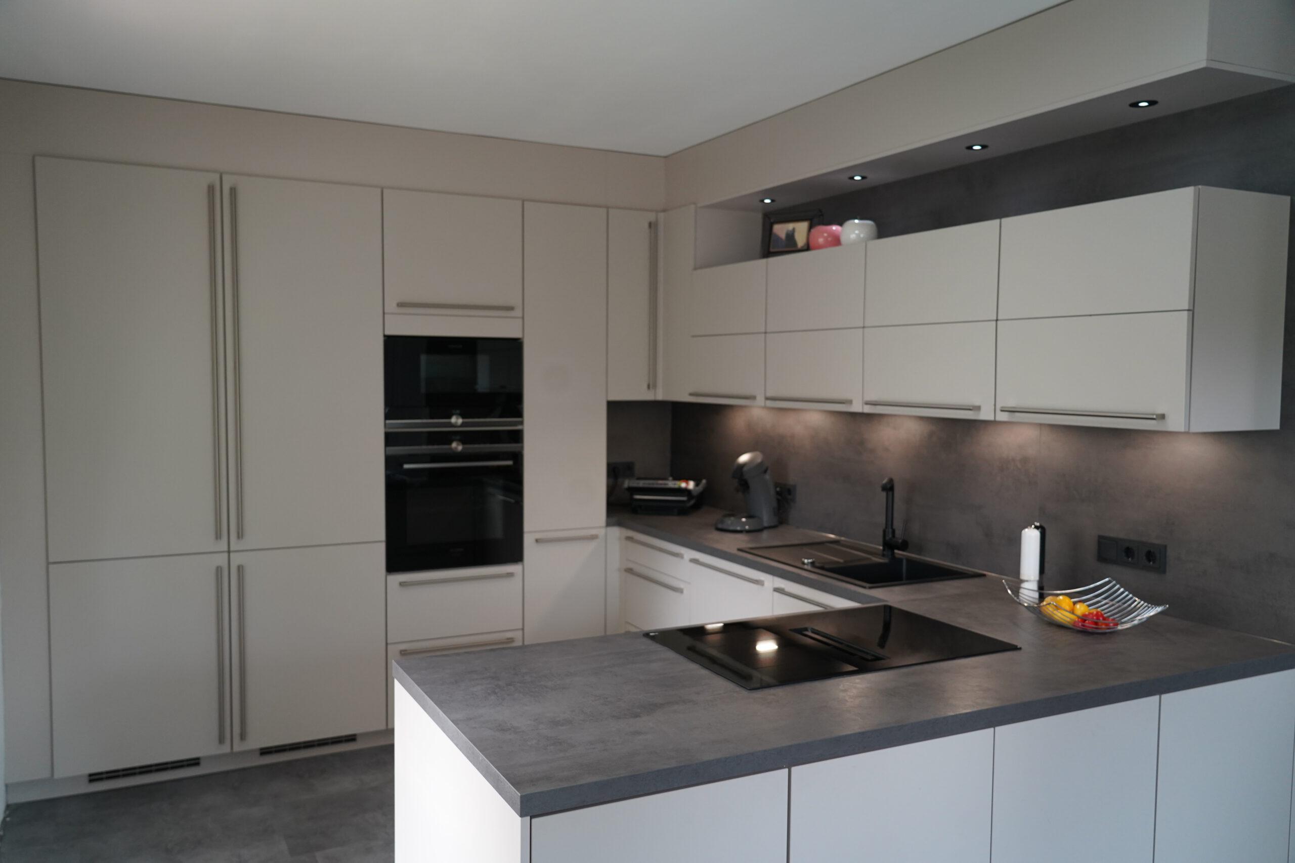 Moderne, minimalistische Küche in Beige und Grau mit eingebauten Geräten und Obstschale als Farbakzent.