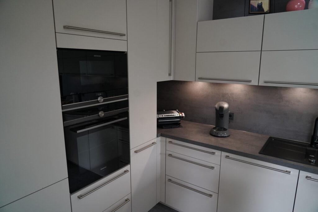 Moderne Küche mit weißen Schränken, grauer Arbeitsplatte, schwarzer Spüle und integrierten Geräten.