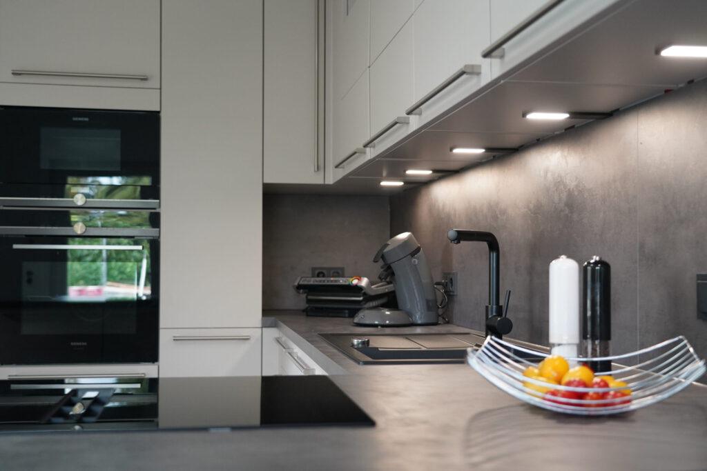 Moderne Küche mit dunkler Arbeitsplatte, eingebautem Backofen, Kaffeemaschine und bunter Obstschale.