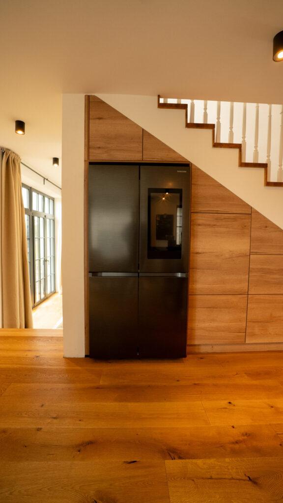 Moderner Innenraum mit Holzfußboden, eingebautem schwarzem Kühlschrank und Treppe darüber.