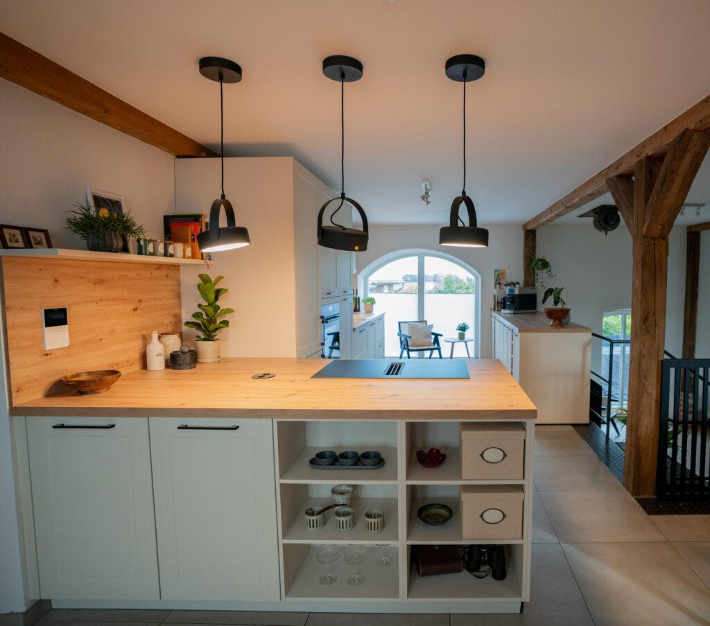 Moderne Küche mit Holzinsel, schwarzen Lampen, Pflanzen und großem Bogenfenster, stilvoll und einladend.