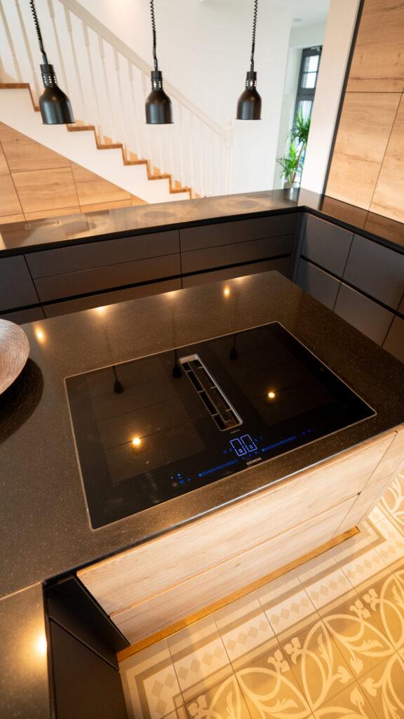 Moderne Küche mit Induktionskochfeld, Holzschränken und schwarzen Arbeitsflächen, warm beleuchtet.