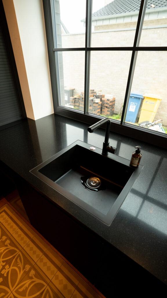 Moderne Küche mit schwarzer Spüle, großem Fenster und Blick auf gestapelte Backsteine und Mülltonnen.