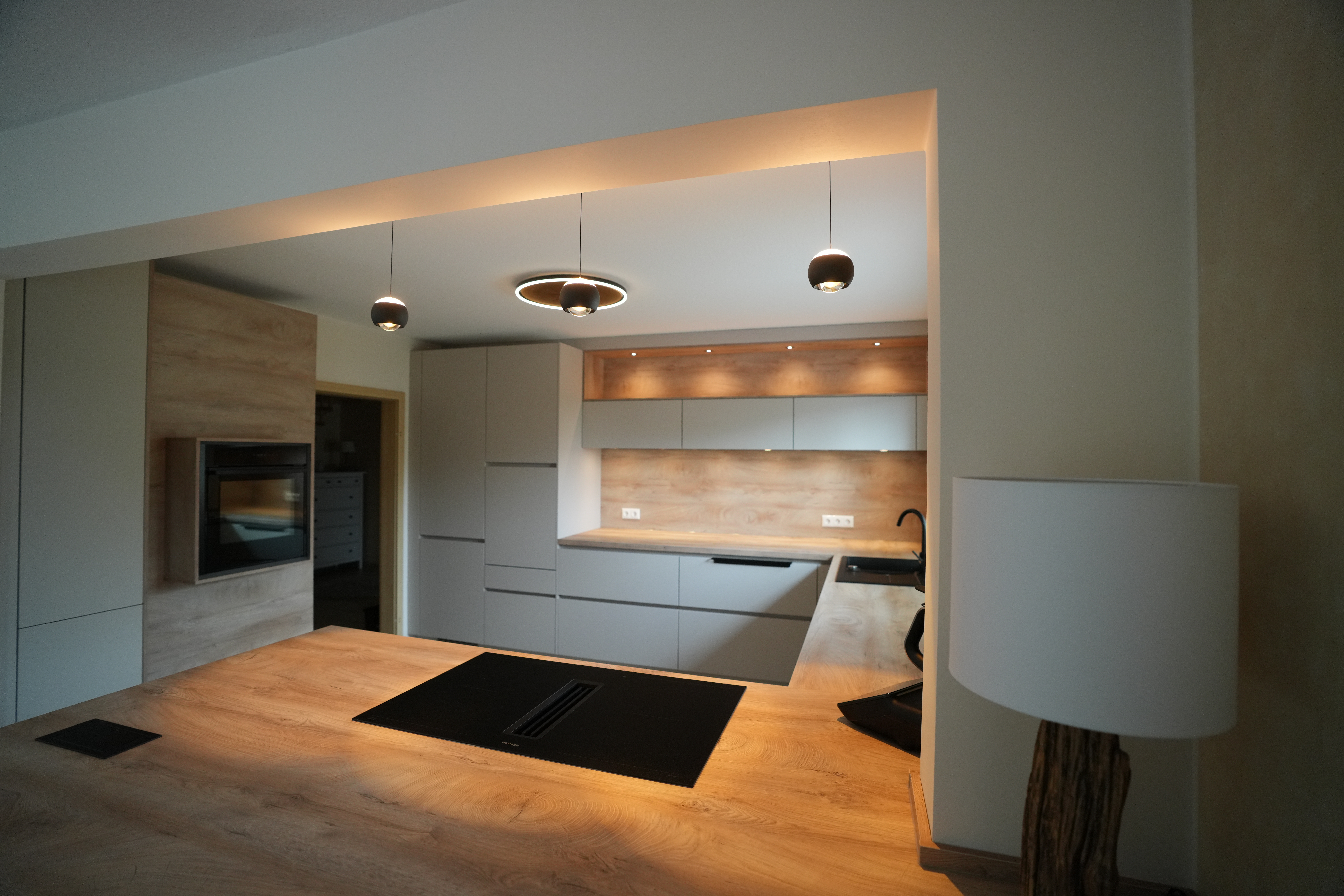 Moderne Küche mit grauen Schränken, Holzarbeitsflächen, Kochfeld, Ofen und Hängelampen.