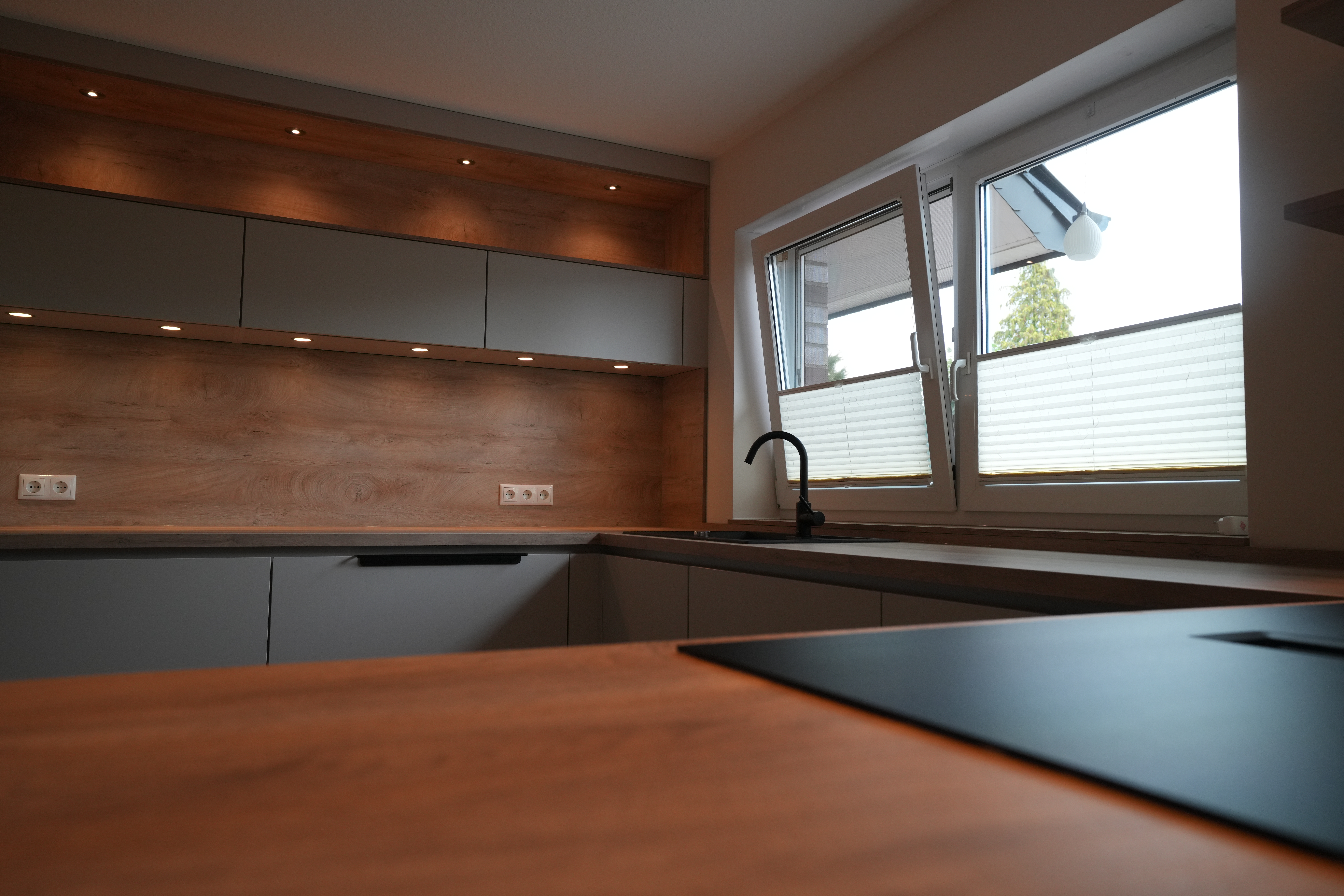 Moderne, saubere Küche mit grauen Schränken, Holzarbeitsplatte und einladendem Tageslicht.