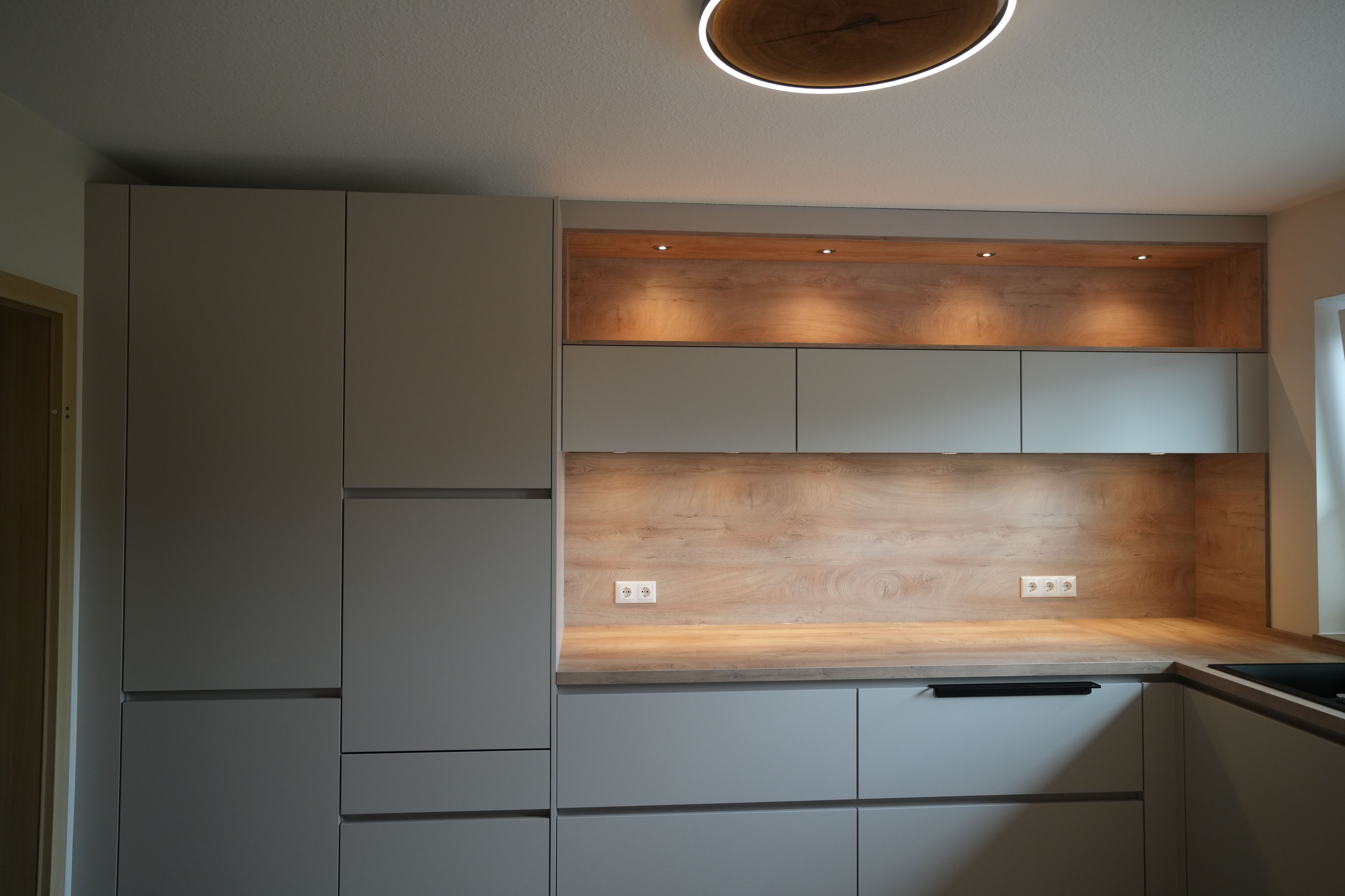 Moderne Küche mit grauen Schränken, Holzarbeitsplatte und integrierter Beleuchtung in minimalistischer Optik.