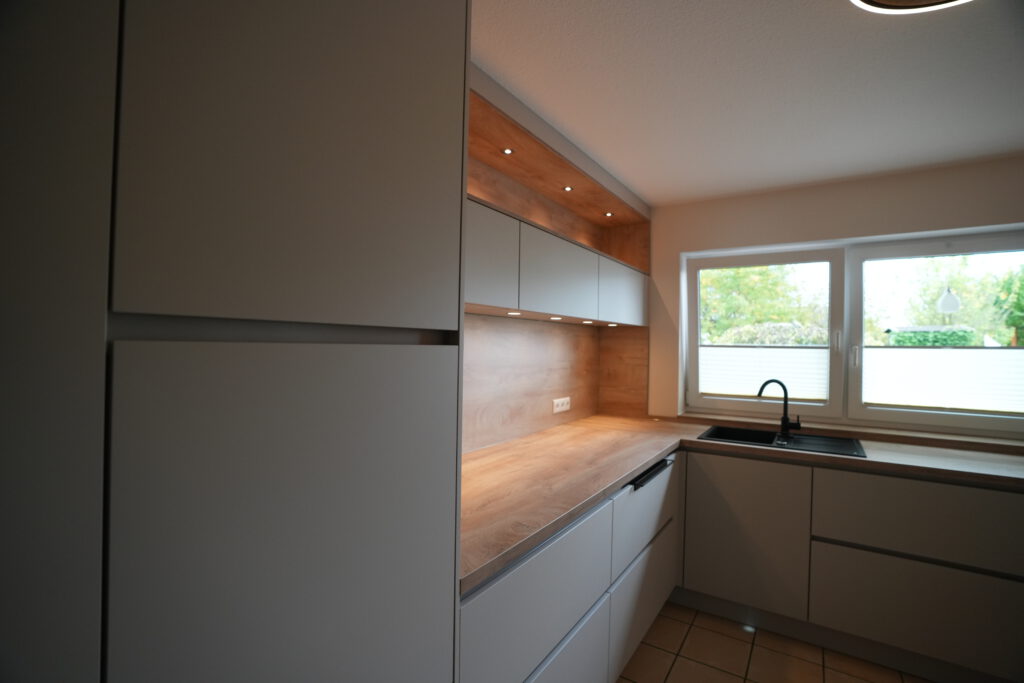 Moderne, aufgeräumte Küche mit grauen Schränken, Holzarbeitsplatte und großem Fenster für viel Licht.