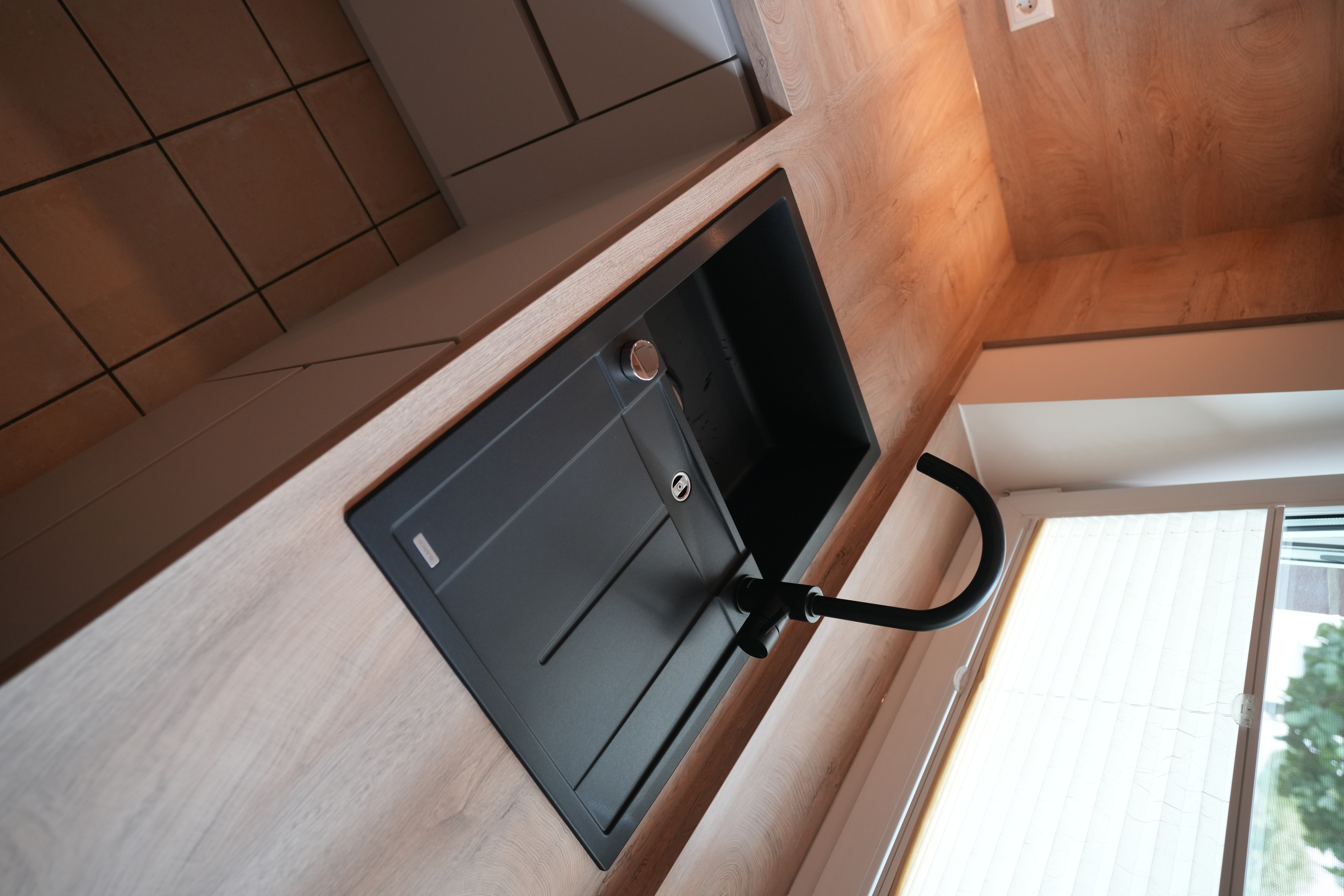Moderne Küchenecke mit schwarzer Spüle, Holzarbeitsplatte und hellem Lichteinfall durch ein Fenster.
