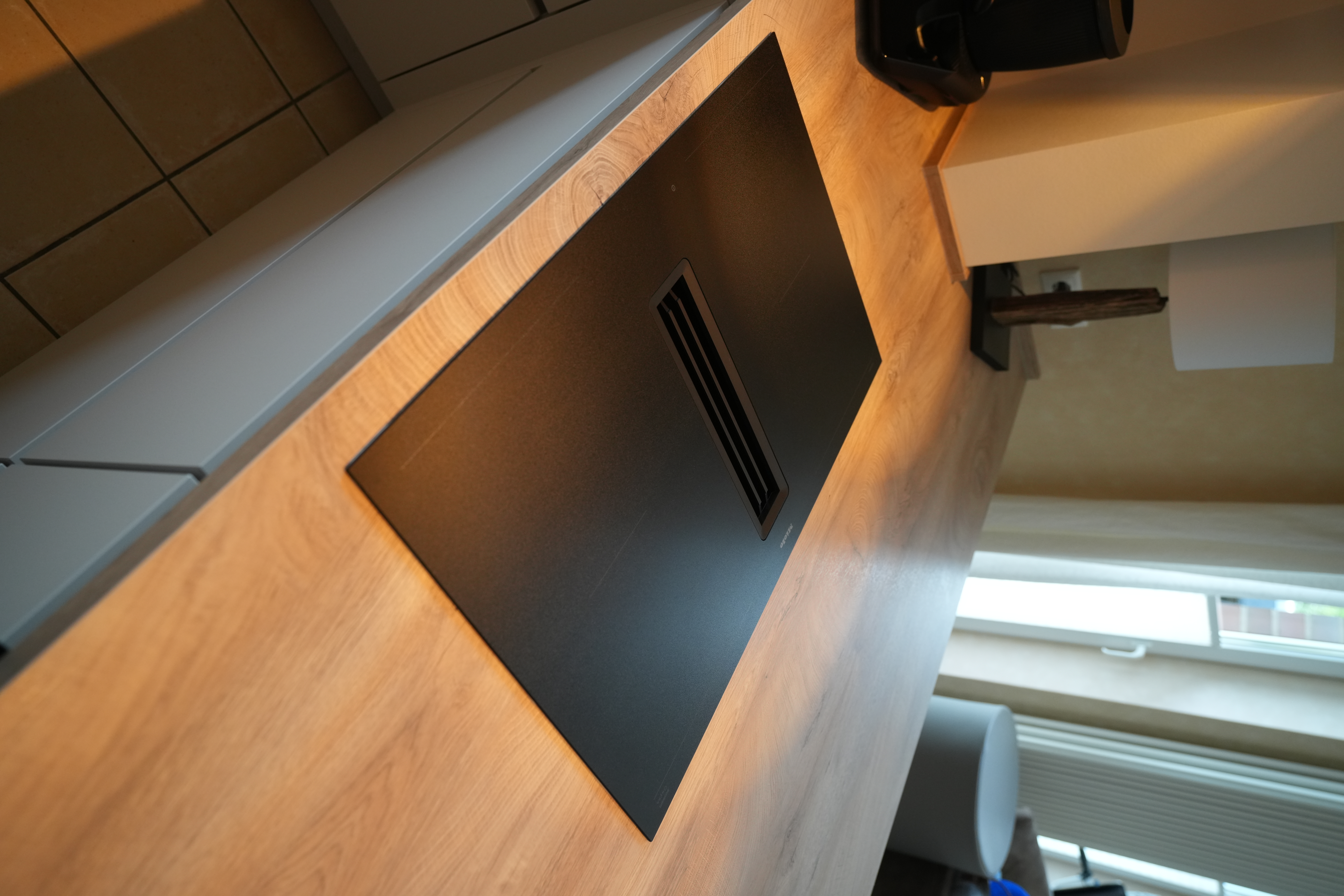 Moderne Küche mit Induktionskochfeld, Holzarbeitsplatte, schwarzer Kaffeemaschine und Tischlampe.