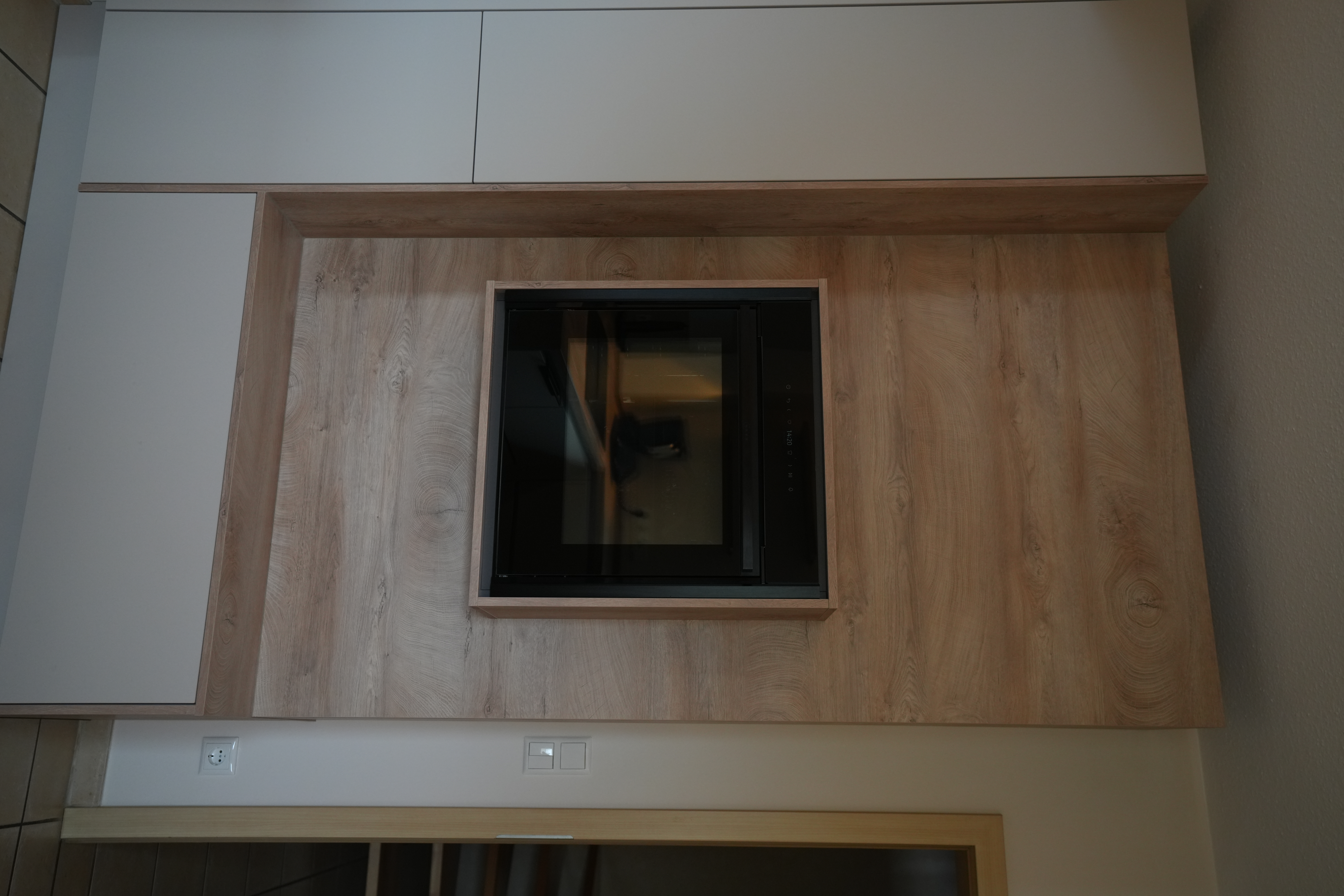 Moderner Küchenbereich mit schwarzem Backofen in Holzverkleidung, hellem Schrank und beigen Fliesen.