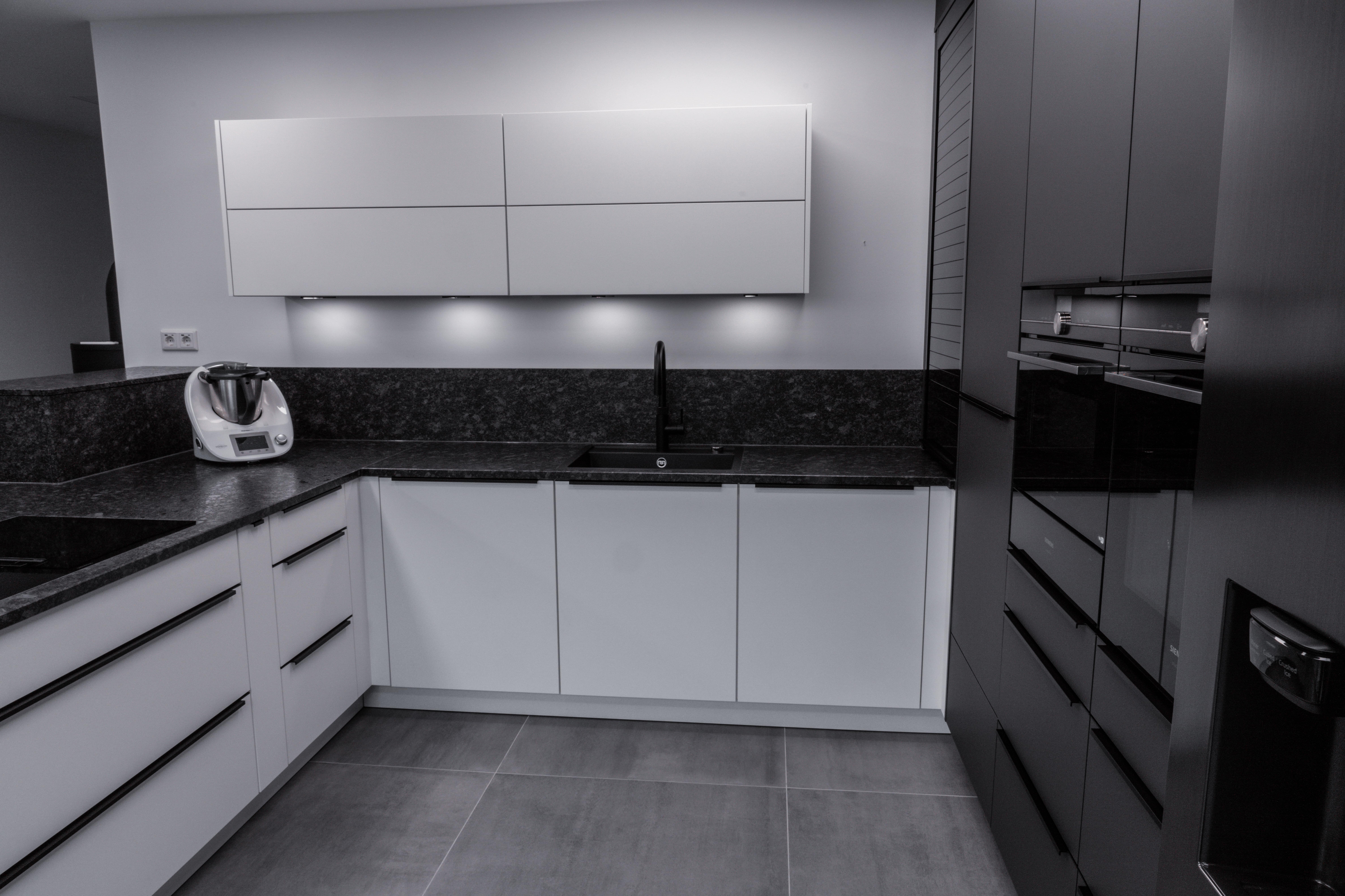 Moderne, minimalistische Küche in Weiß und Grau mit dunkler Arbeitsplatte und eingebauten Geräten.