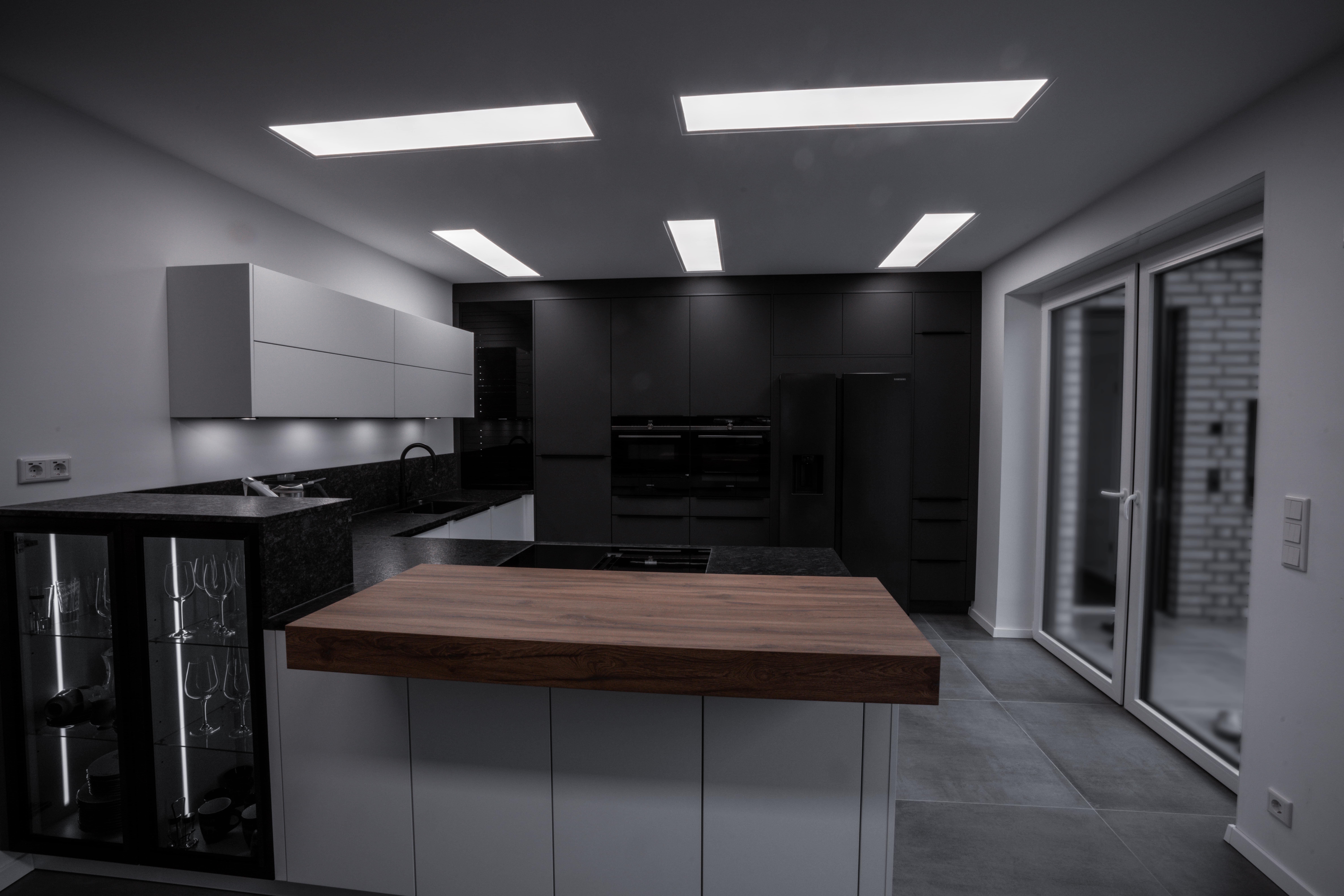 Moderne, unbenutzte Küche mit dunklen Schränken, Holzinsel und klarer Beleuchtung. Elegantes Design.